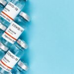 Array of COVID-19 vaccine vials on a blue surface, offering ample copy space.