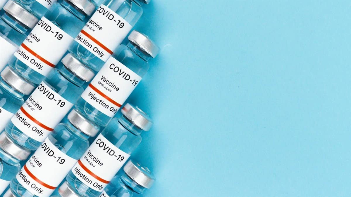 Array of COVID-19 vaccine vials on a blue surface, offering ample copy space.