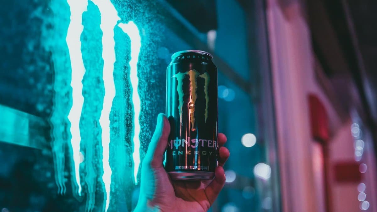 Energy drink can held against neon-lit urban backdrop. Night shot with vivid colors.