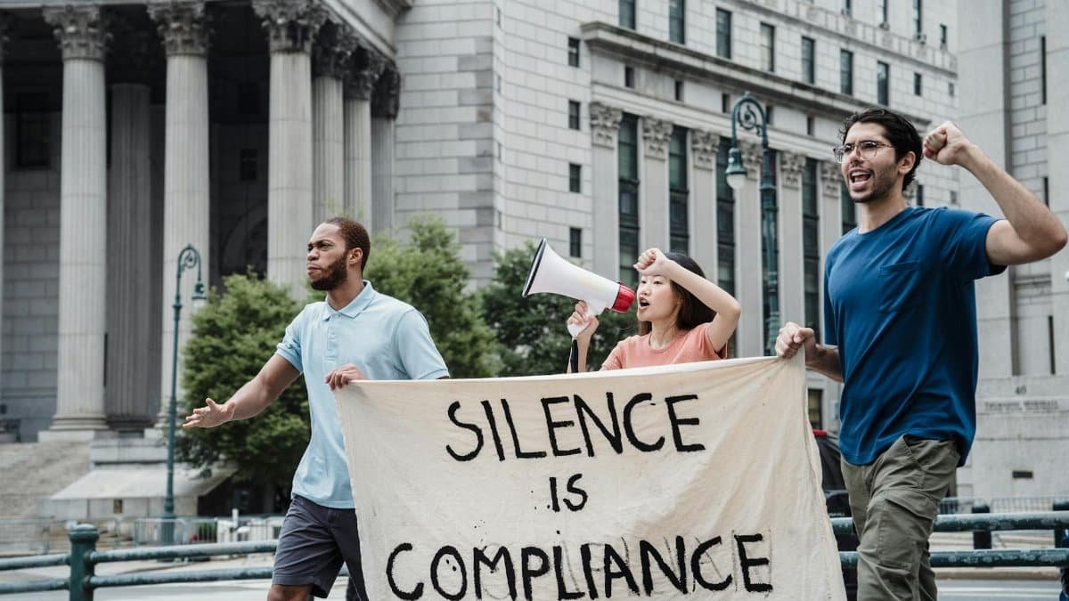 Activists marching with a banner saying 'Silence is Compliance' outside a courthouse.