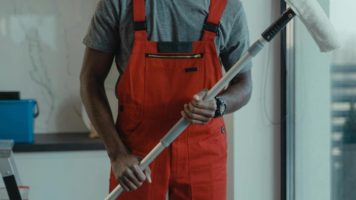 A professional cleaner wearing red overalls is holding a mop while cleaning indoors.