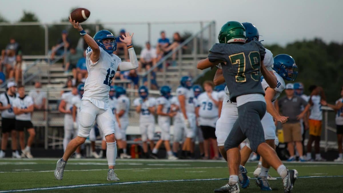 High school football game with quarterback throwing a pass under pressure.