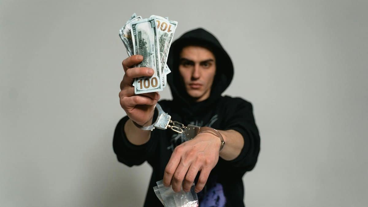 Close-up of a man in handcuffs holding cash and drugs, illustrating crime and illegal activities.