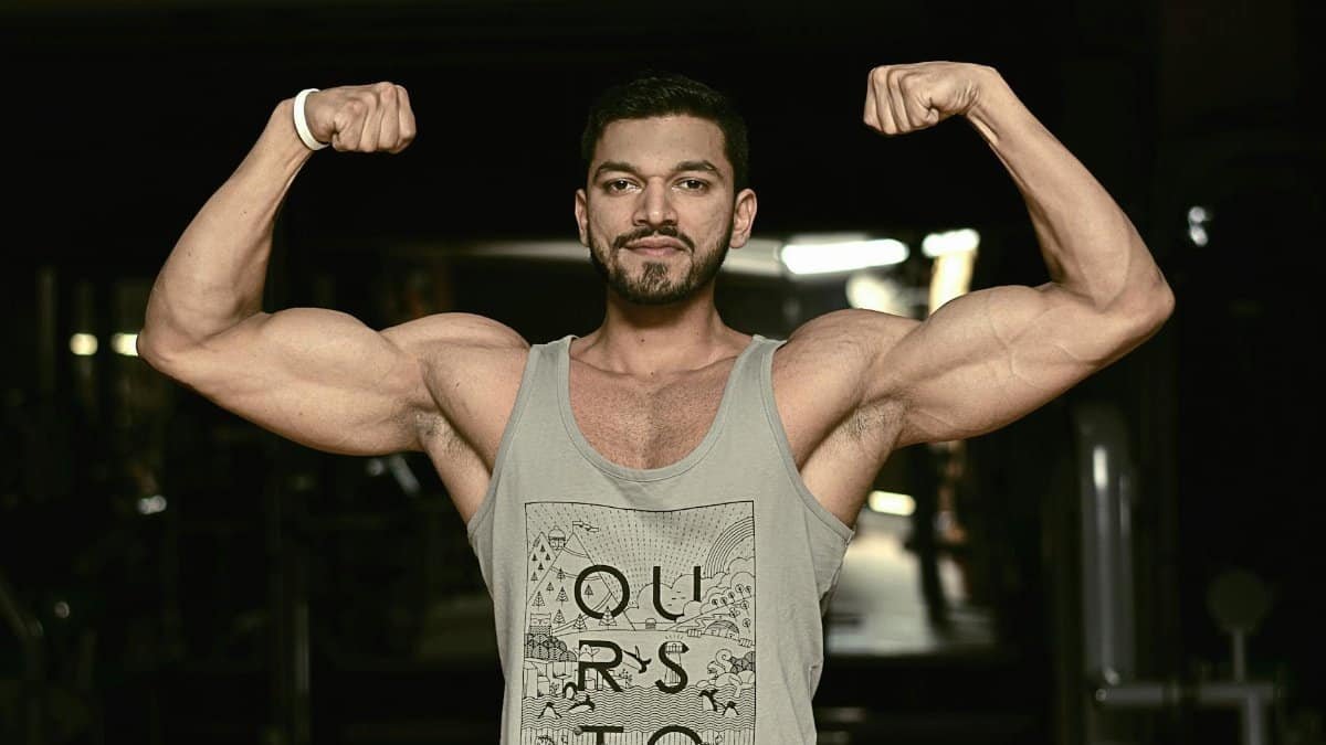 A fit man flexing his biceps in a gym environment, showcasing strength and fitness.