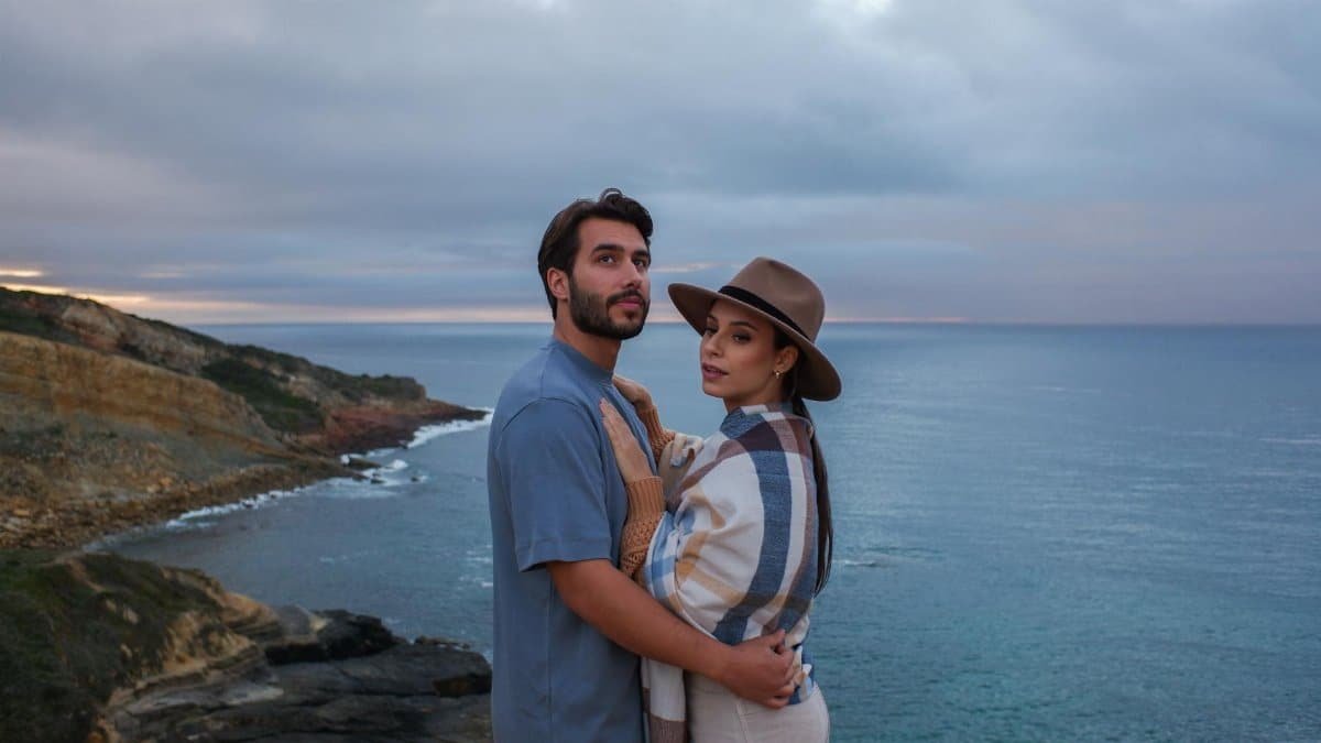 A couple embraces on a scenic ocean cliff at sunset, sharing a romantic moment.
