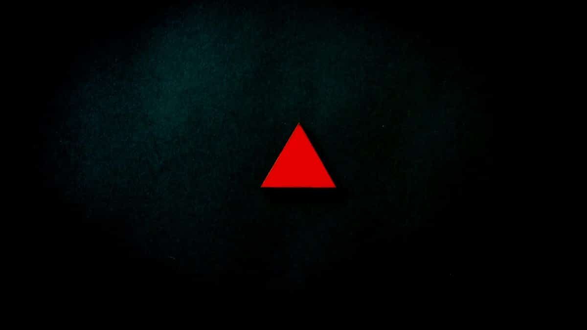 A striking minimalist image of a red triangle centered on a dark, textured background.