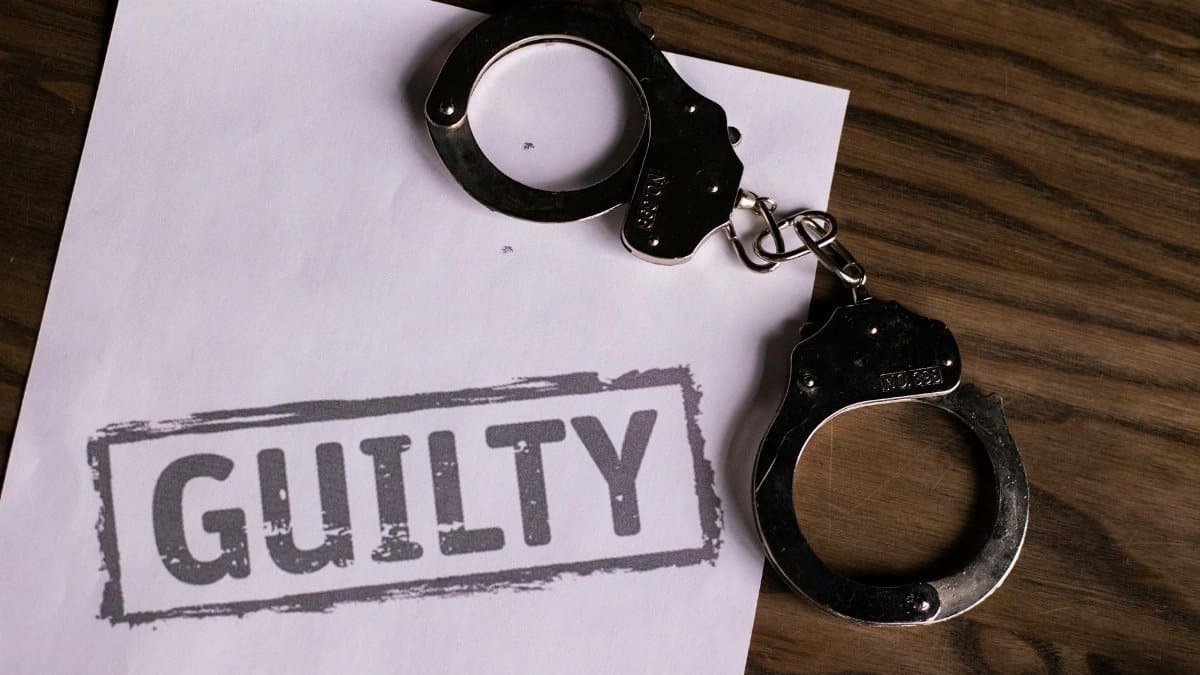 Top view of handcuffs on paper with 'GUILTY' text, symbolizing a verdict or crime.