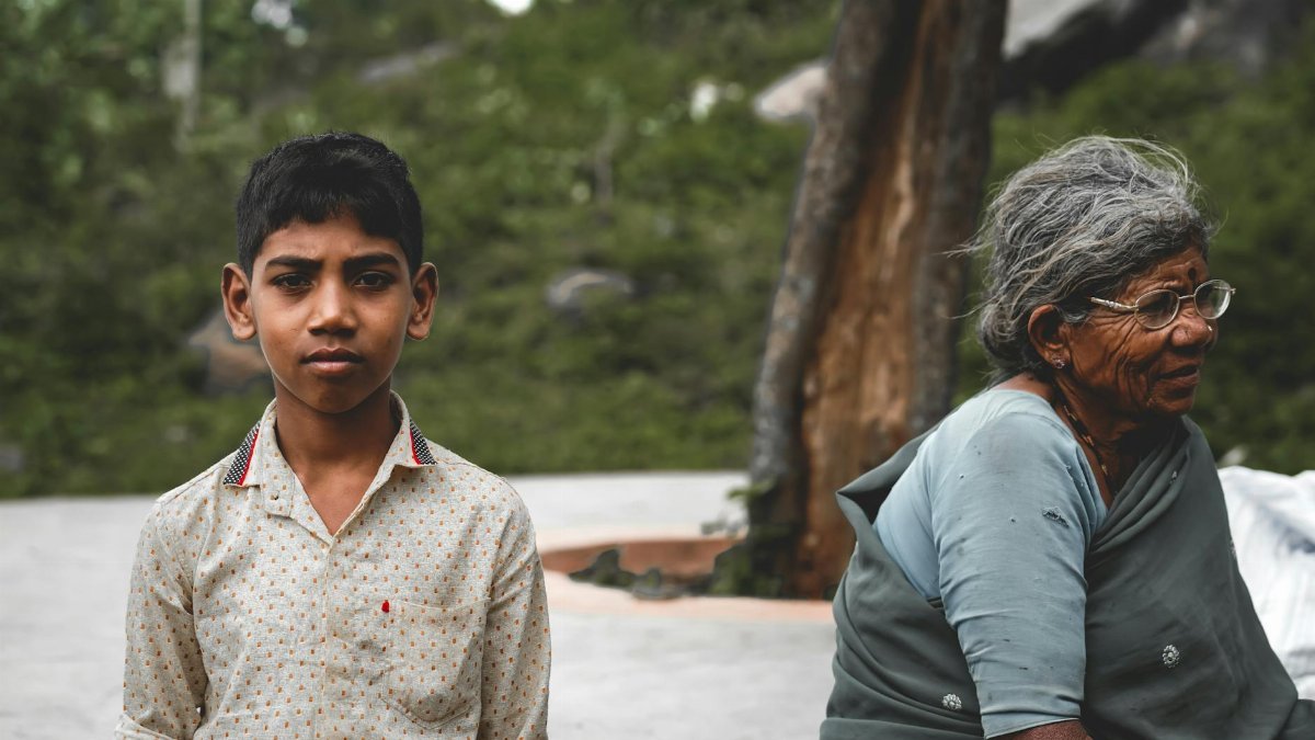 A senior woman and a young boy outdoors in a rural setting, conveying bond across generations.