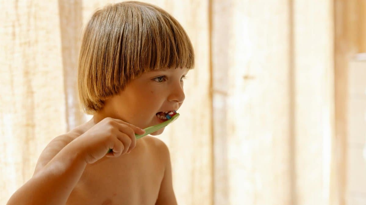 Young boy brushing teeth indoors in soft natural light, promoting dental care routines.