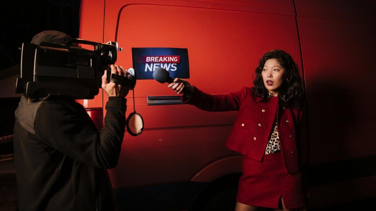 Asian female reporter with cameraman conducting a nighttime news broadcast beside a news van.