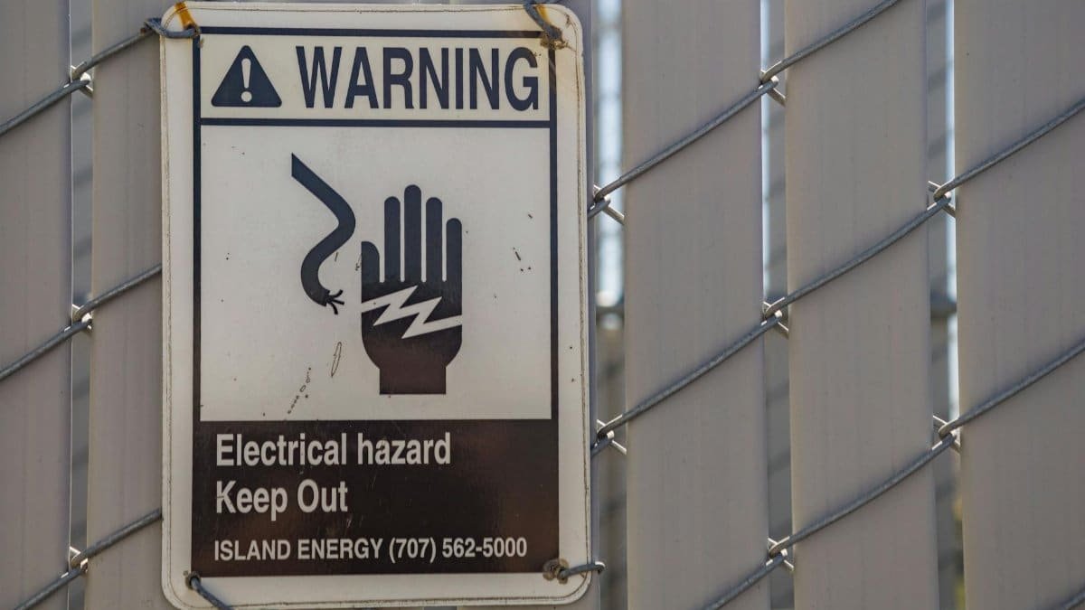 Close-up of a warning sign for electrical hazards on a chain-link fence.