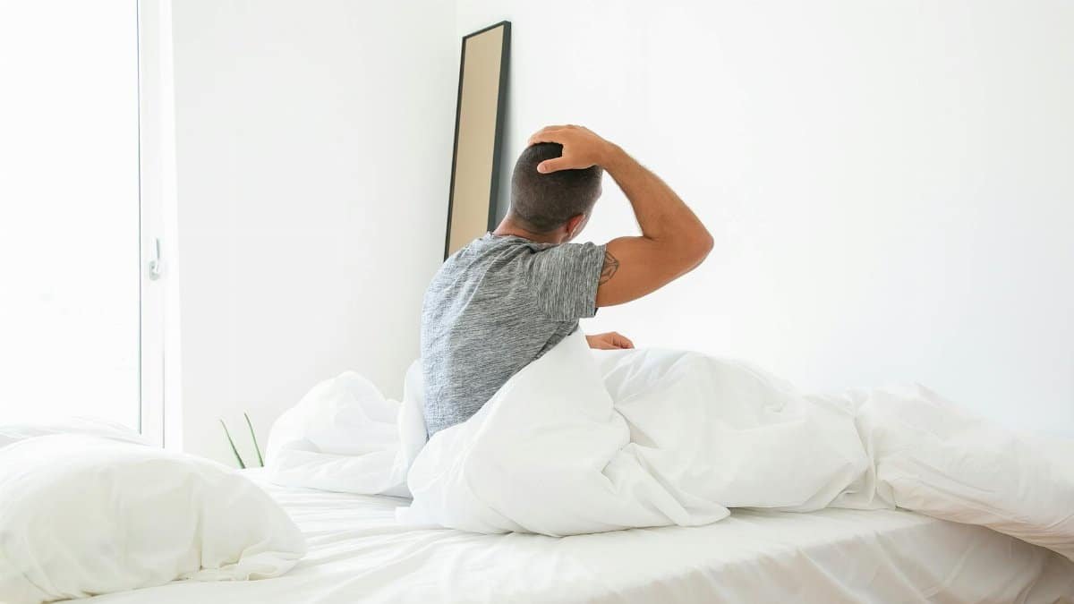 A man stretches in bed during a bright morning, starting his day.