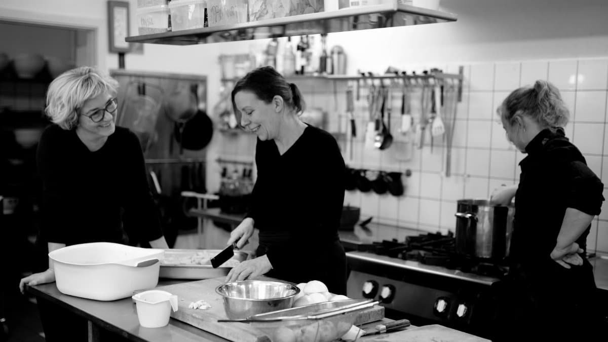 Black and white company of female cooks preparing food in kitchen of cafe while interacting and smiling
