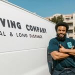A cheerful mover standing confidently beside a moving company's van, ready for local or long distance relocation services.