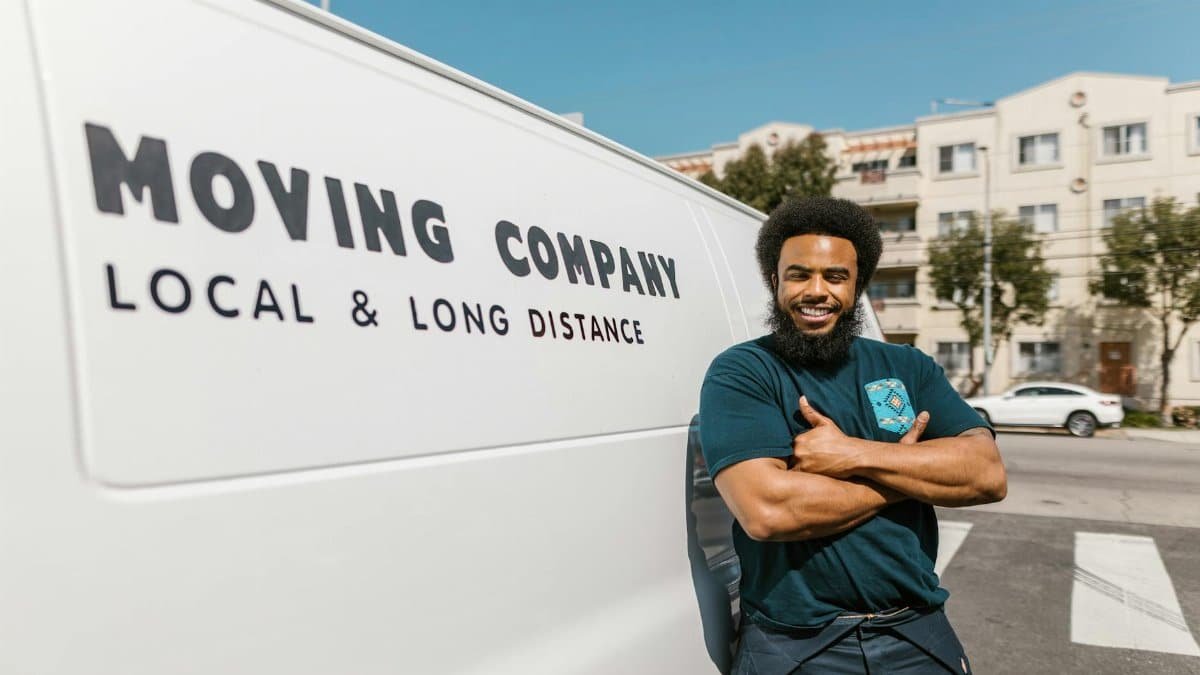 A cheerful mover standing confidently beside a moving company's van, ready for local or long distance relocation services.