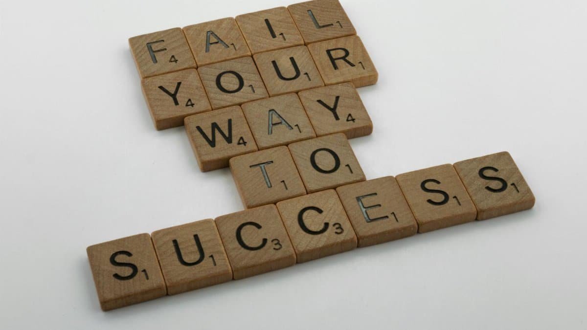 Wooden tiles spell 'Fail Your Way to Success' emphasizing perseverance.