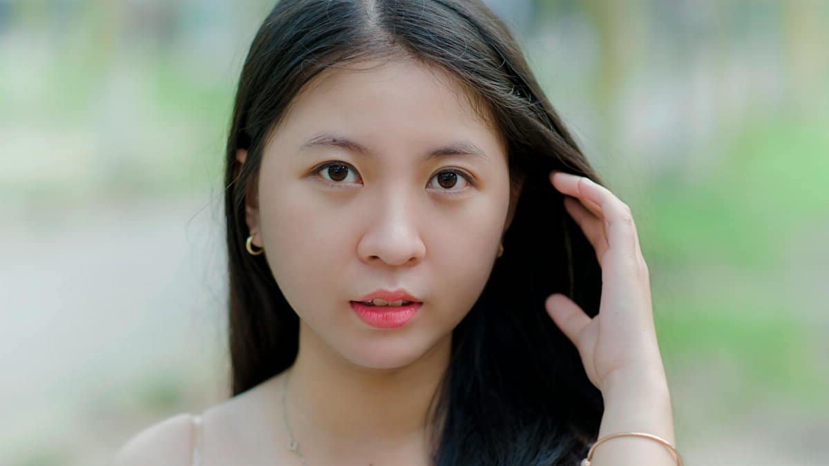 Portrait of a young woman with long dark hair, standing outdoors, looking directly at the camera.