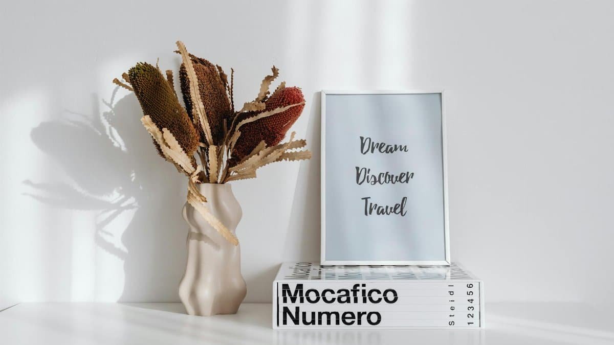 Simple still life with framed text, dry plant, and books on white background.