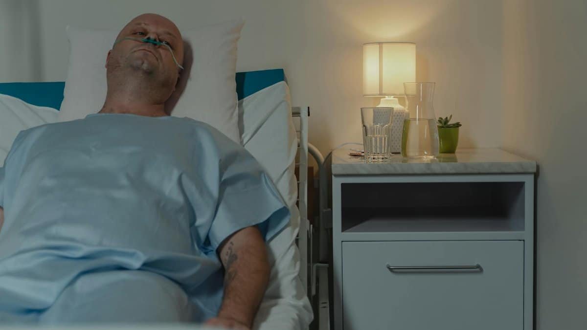 A man lying in a hospital bed with a nasal cannula, illuminated by bedside lamp.