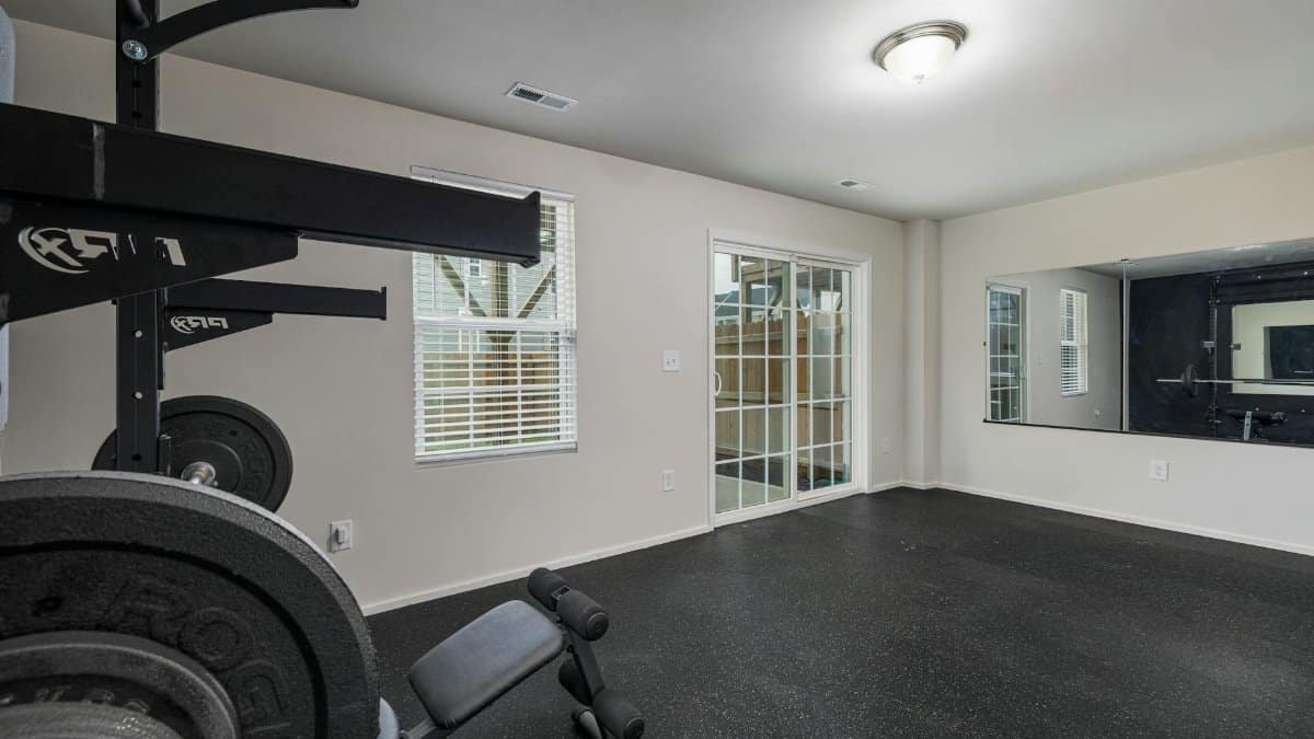 A well-lit, spacious home gym featuring modern weightlifting equipment and a large mirror.