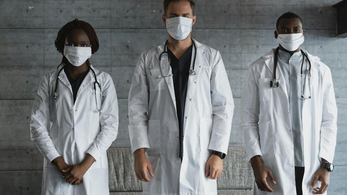 A diverse group of doctors in white coats and masks standing indoors, signifying unity in healthcare.