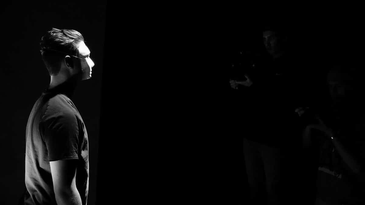 A moody black and white portrait of a man in a spotlight, with a dark background and dramatic lighting.