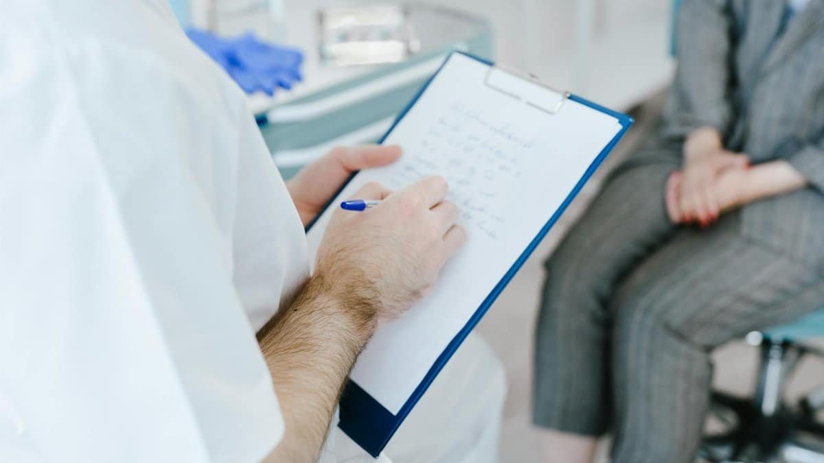 Medical professional writing patient notes on clipboard during consultation.