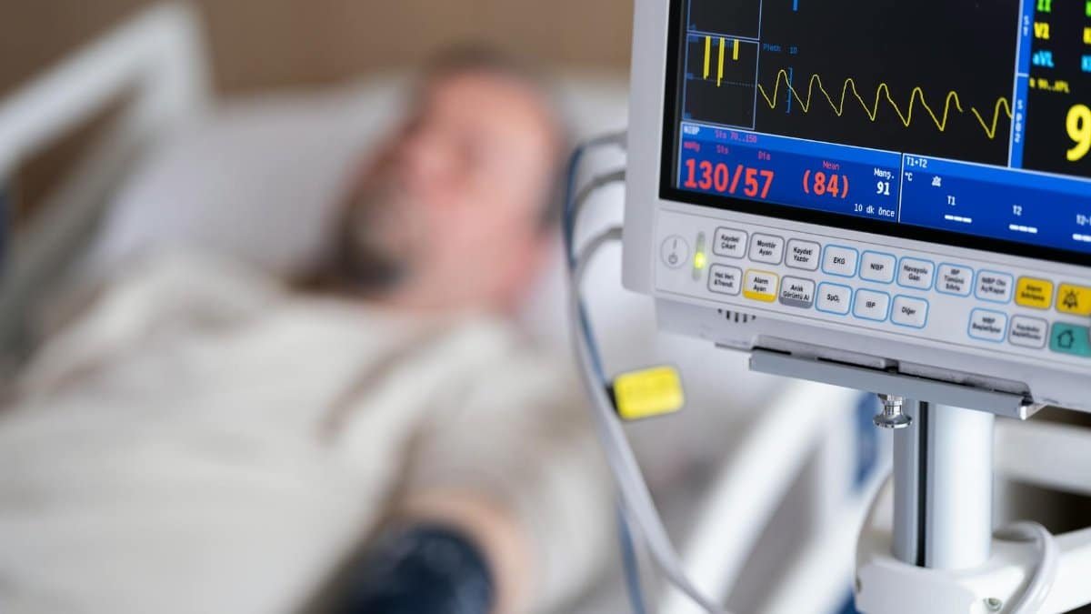 Patient in hospital bed with heart monitor showing blood pressure and heart rate.