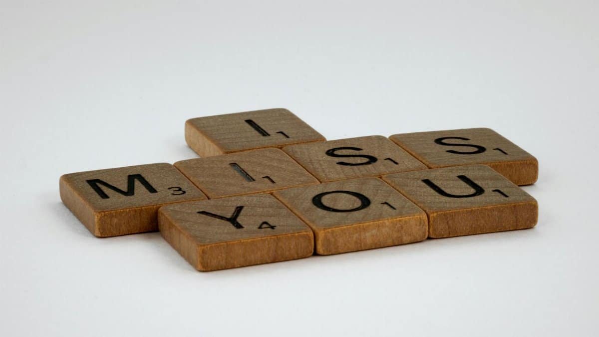Close-up of Scrabble tiles spelling 'I Miss You' on a white surface with ample copy space.
