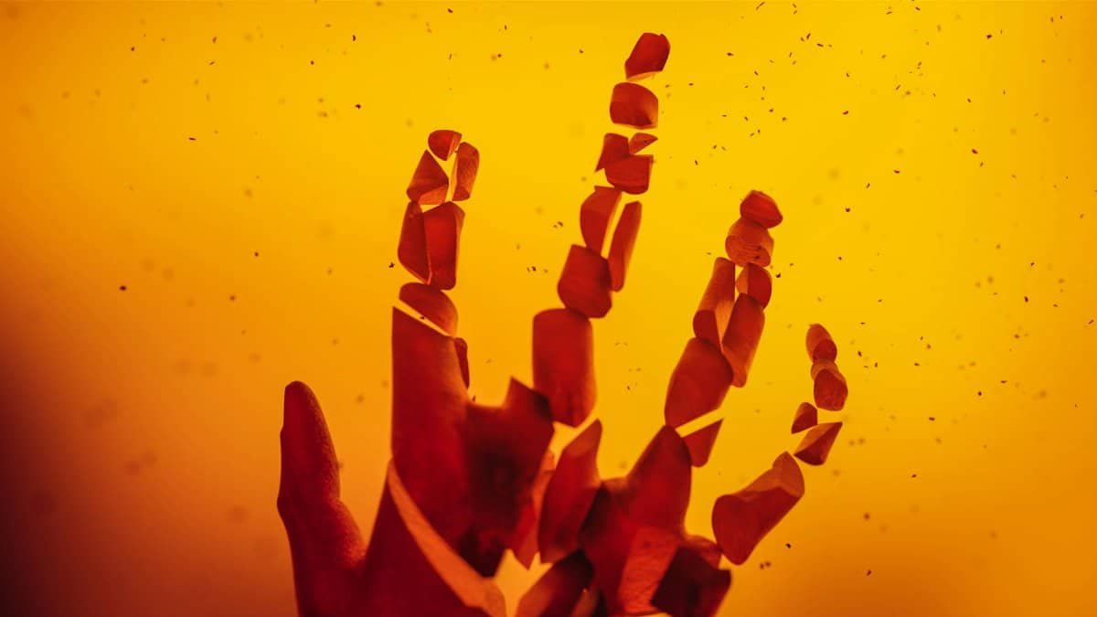 An abstract representation of a hand disintegrating into pieces against a warm, orange backdrop.