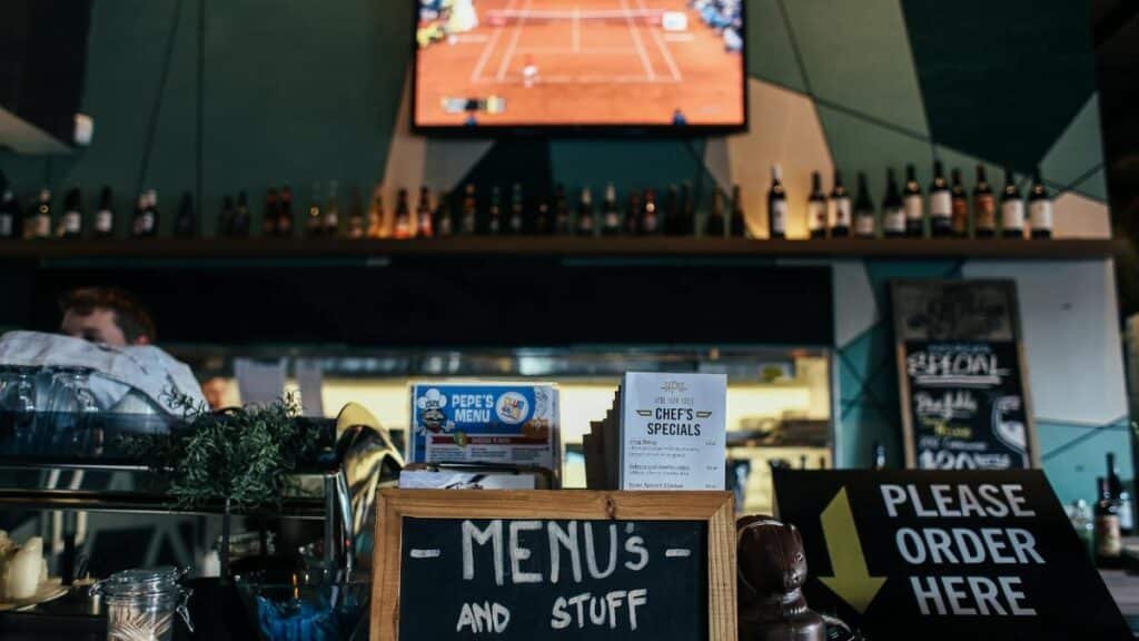 A lively bar scene with menus and bottles, featuring a TV showing sports.