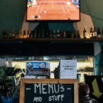 A lively bar scene with menus and bottles, featuring a TV showing sports.