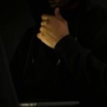 A man in a hoodie uses a laptop in darkness, symbolizing cybercrime and anonymity.