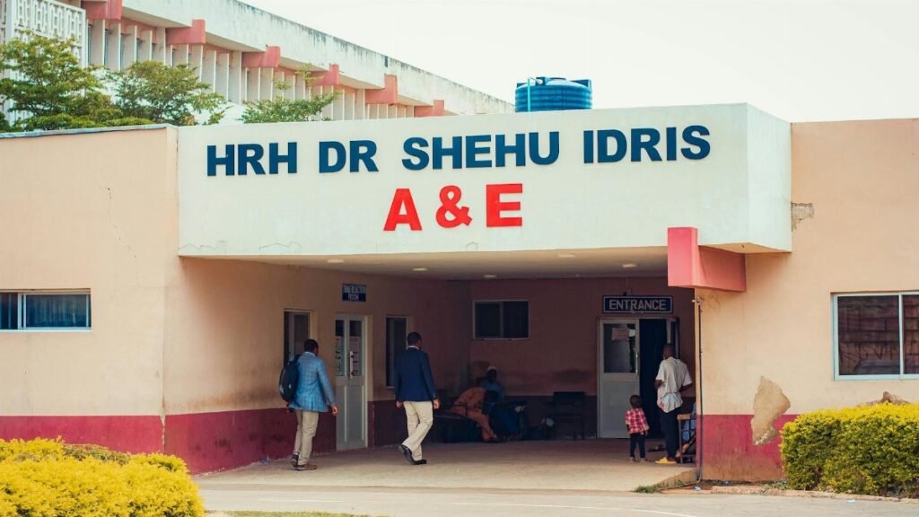 Visitors entering HRH Dr Shehu Idris A&E, capturing outdoor hospital scene with people.