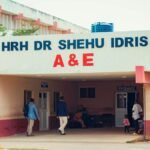 Visitors entering HRH Dr Shehu Idris A&E, capturing outdoor hospital scene with people.