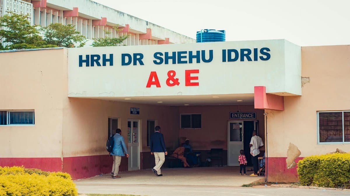 Visitors entering HRH Dr Shehu Idris A&E, capturing outdoor hospital scene with people.