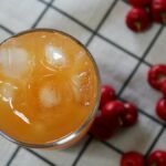 Overhead view of refreshing cherry juice with ice and fresh cherries on checkered cloth.