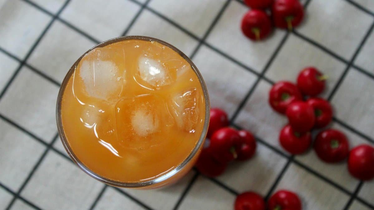 Overhead view of refreshing cherry juice with ice and fresh cherries on checkered cloth.