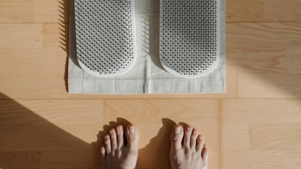 Close-up of bare feet on a wooden floor with acupressure mat, highlighting relaxation therapy.