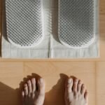 Close-up of bare feet on a wooden floor with acupressure mat, highlighting relaxation therapy.