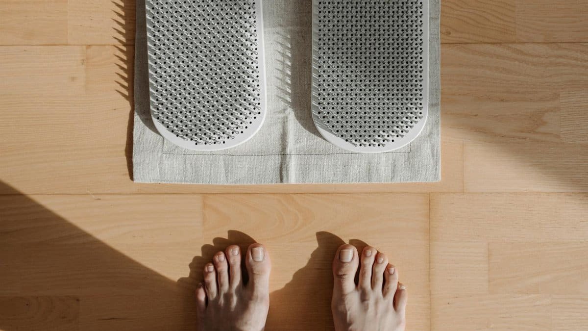 Close-up of bare feet on a wooden floor with acupressure mat, highlighting relaxation therapy.