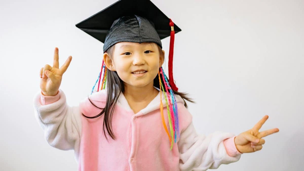 A cheerful child in a graduation cap expressing happiness and success while making peace signs.