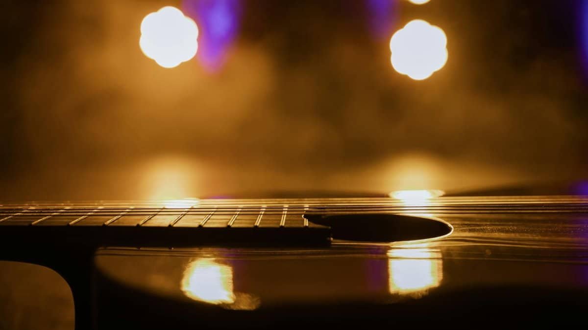 Close-up view of an acoustic guitar in warm, dramatic lighting with light reflections.