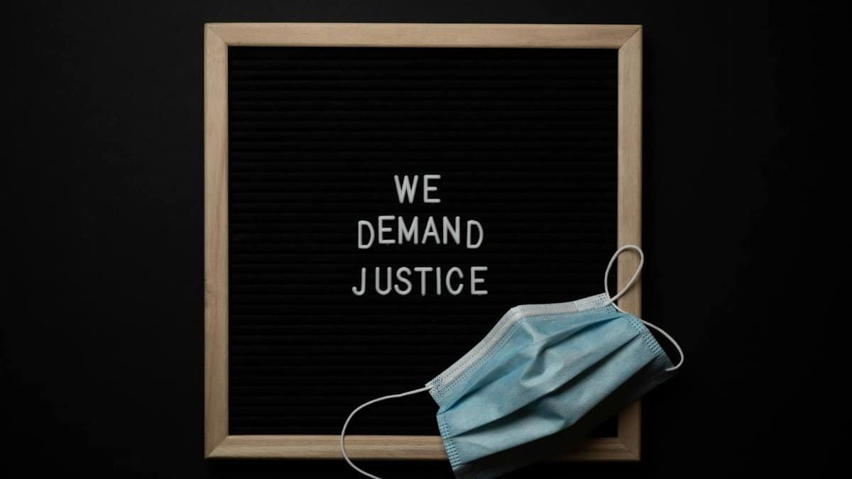 Top view arrangement of protective face mask placed on black framed image with bright white text We Demand Justice on black background