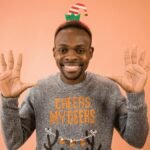 Portrait of a smiling man wearing a festive sweater and elf hat, spreading holiday cheer.