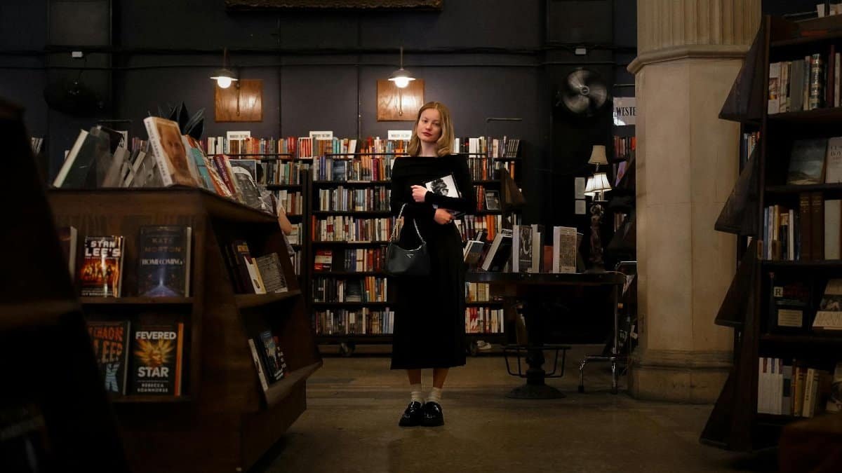 A young woman stands in a cozy bookstore surrounded by shelves filled with books, creating a literary ambiance.