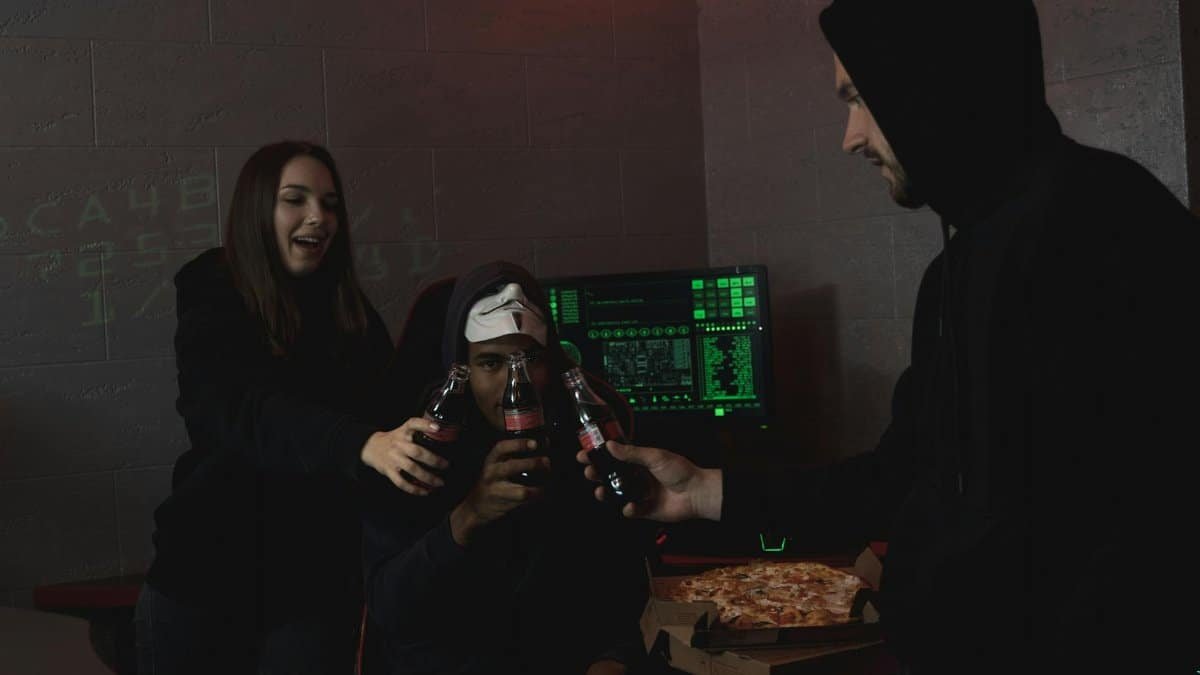 Group of hackers celebrating a successful hack with pizza and soda indoors.