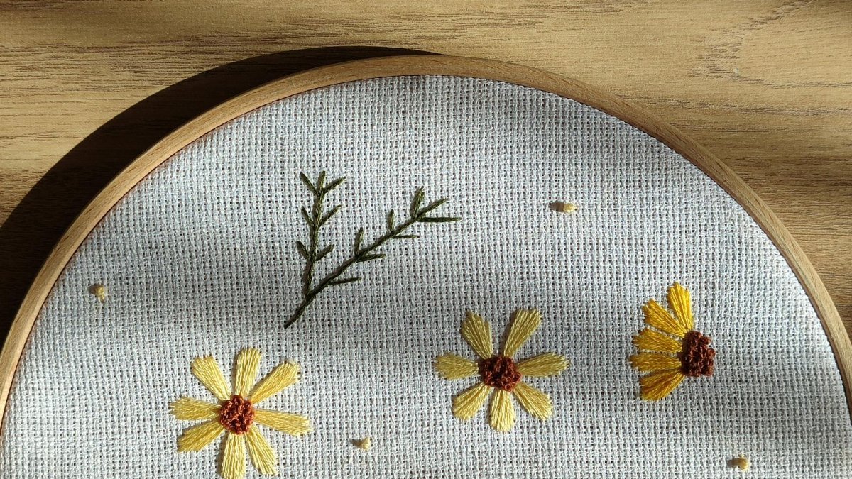 Beautiful embroidery of yellow flowers on canvas, framed in a wooden hoop with natural light.