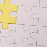 Close-up of a white jigsaw puzzle with a single yellow piece missing, symbolizing incompleteness.