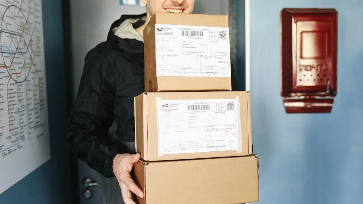 Smiling delivery man holding packages inside a building, ready for delivery.